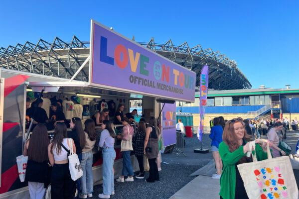 Pop up merchandise stand for Harry Styles, fan holding tote bag very happy.