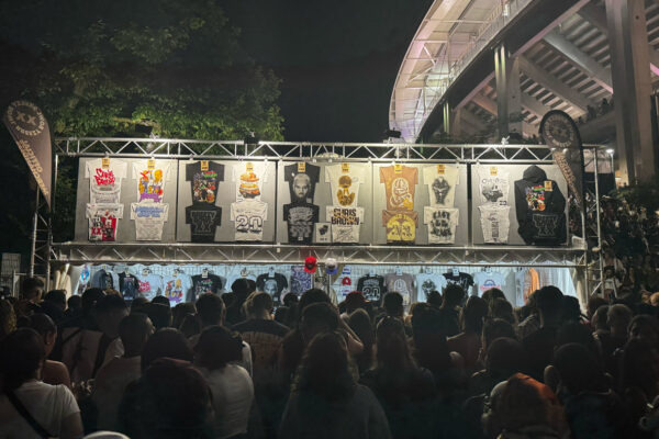 Long shot of Chris Brown merchandise stand with crowd and t shirts displayed above.
