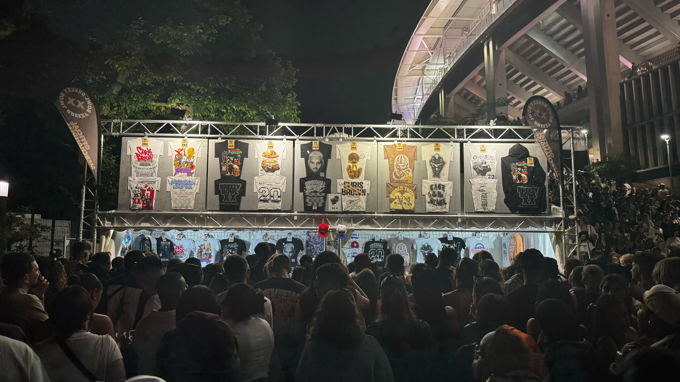 Long shot of Chris Brown merchandise stand with crowd and t shirts displayed above.